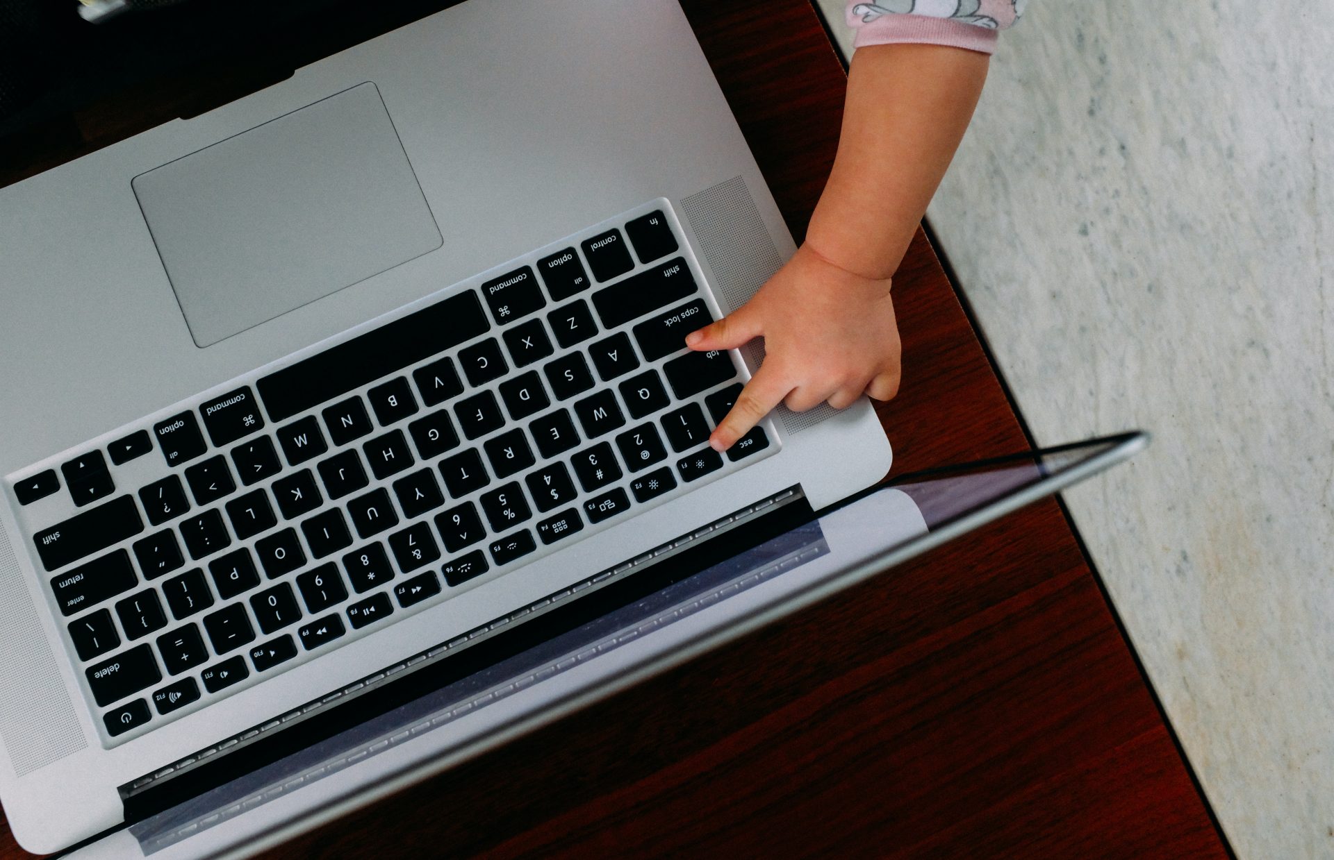 child's hand reaches out to touch a laptop keyboard