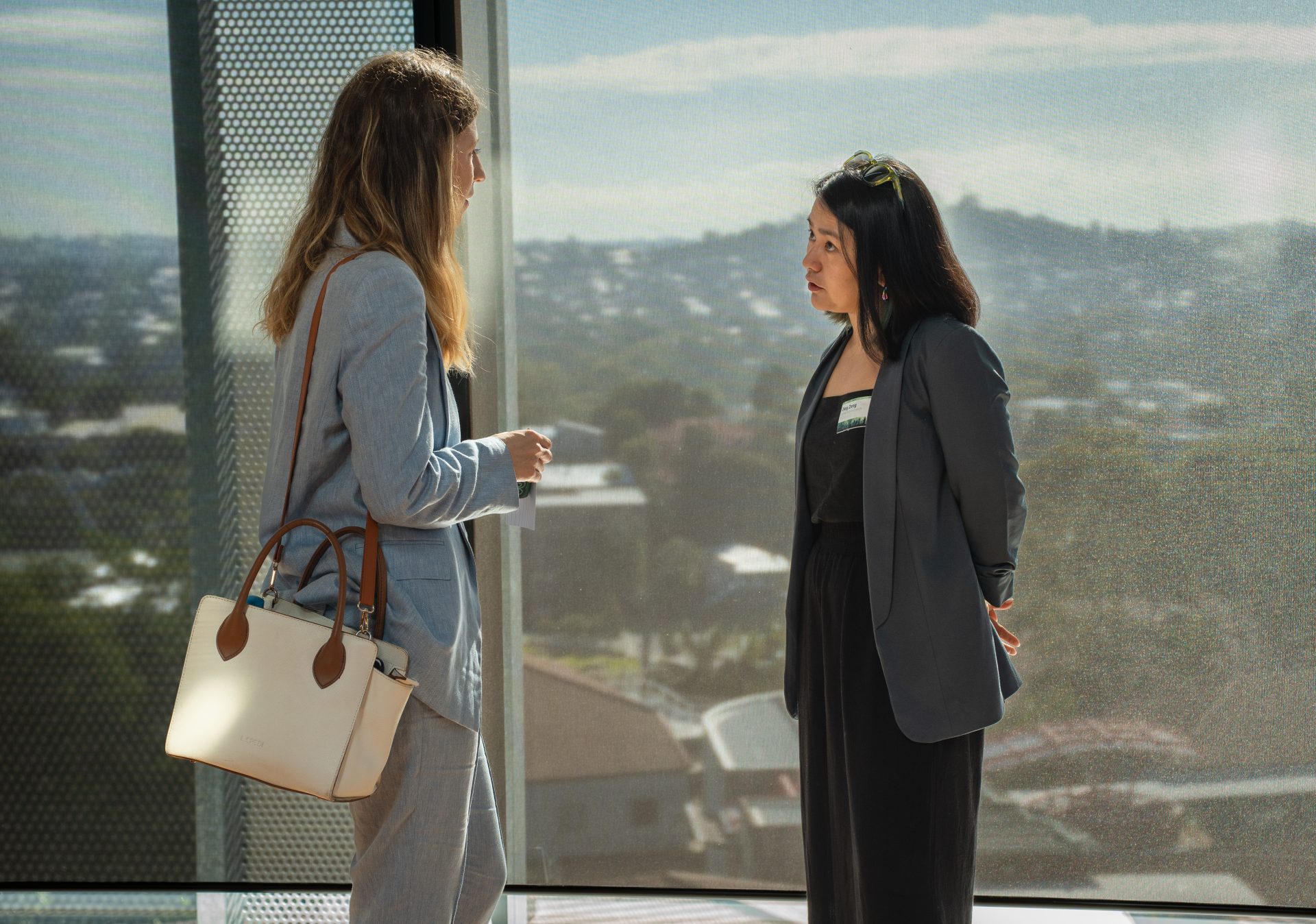 Two women conversing: one wearing a light blue coat and the other in a dark gray coat.