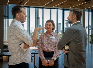 A group of two men and one woman having a conversation: man one in a patterned shirt, man two in a coat, and the woman in a colorful top.