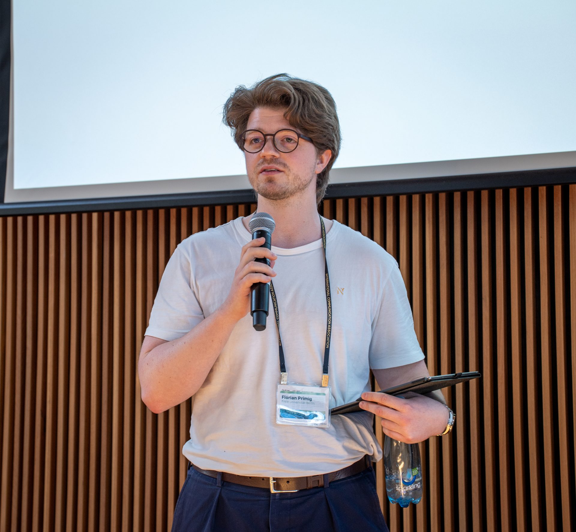 A man with glasses holding a microphone and a tablet.