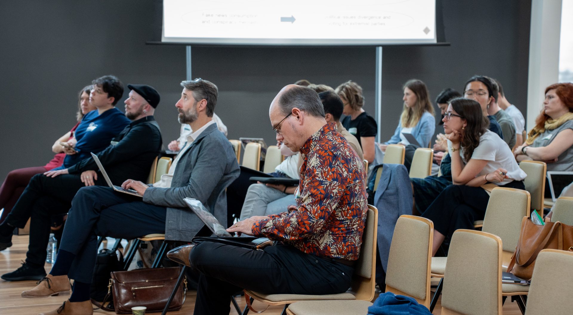 An audience listening attentively to a presentation, with some taking notes.