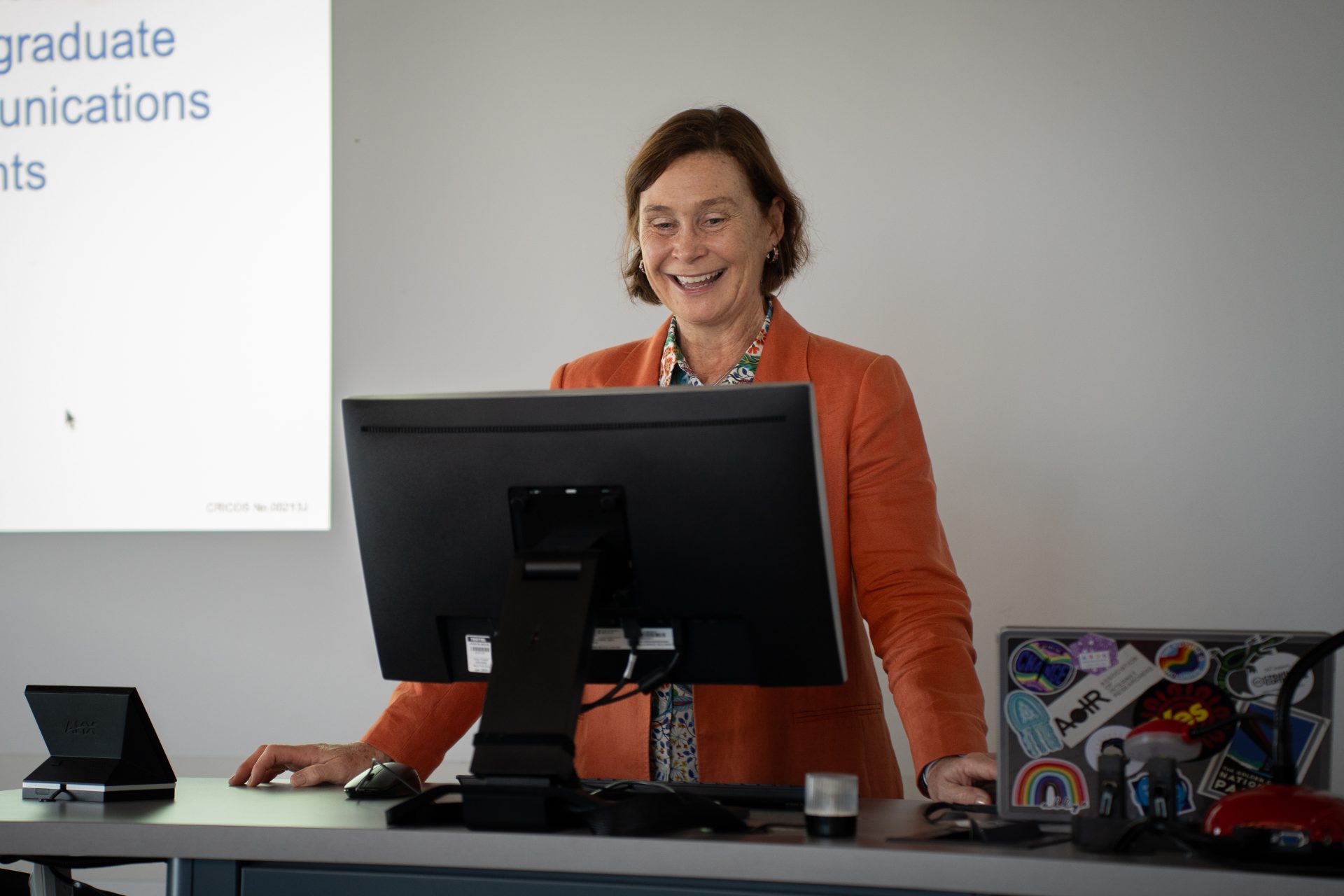 A woman wearing an orange coat looking at a computer screen while giving a presentation.