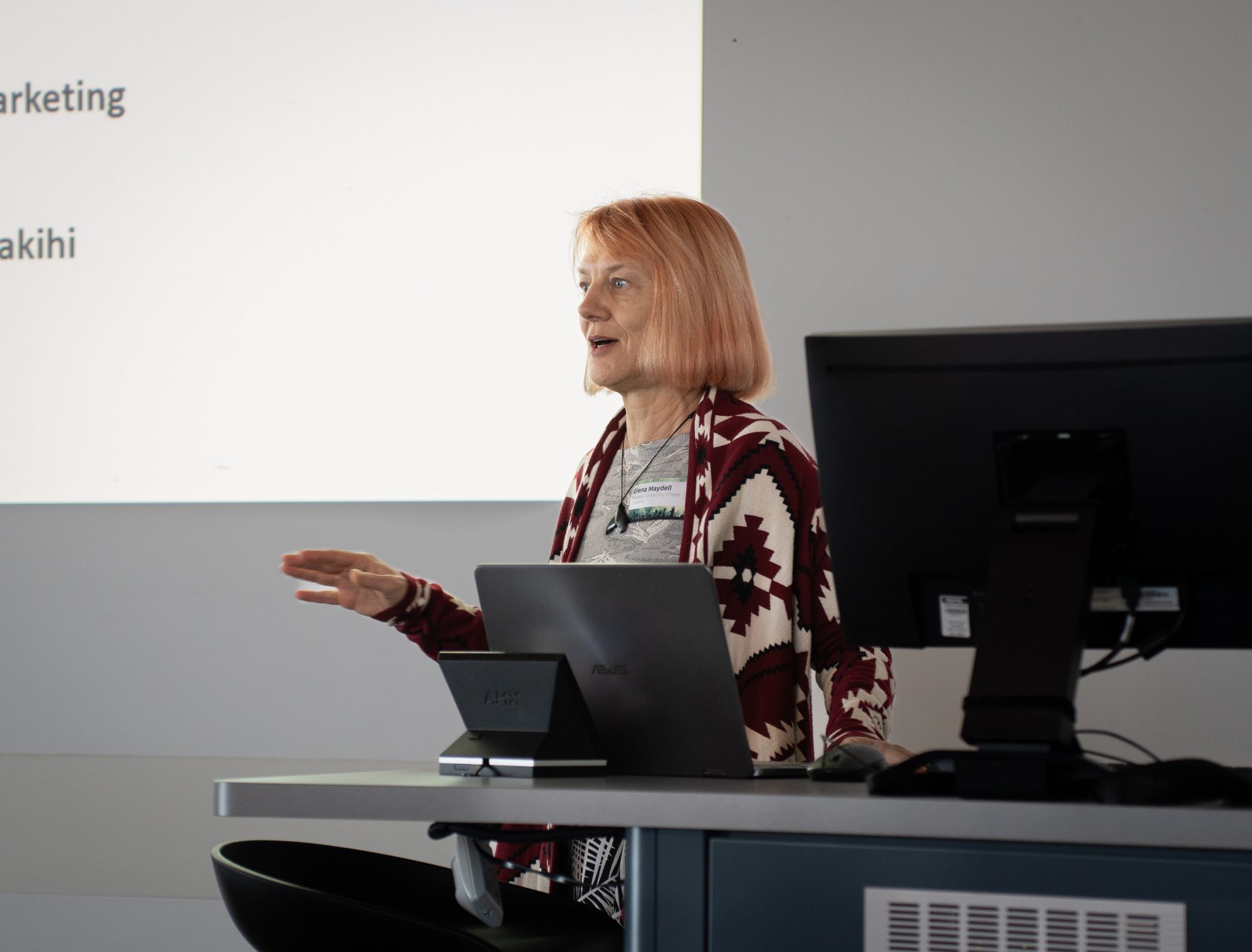 A woman wearing a patterned coat gesturing while giving a presentation.