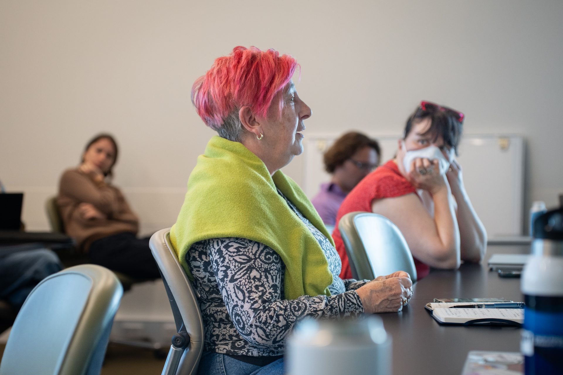 An audience member wearing a green sweater speaking, other audience members seen in the background.