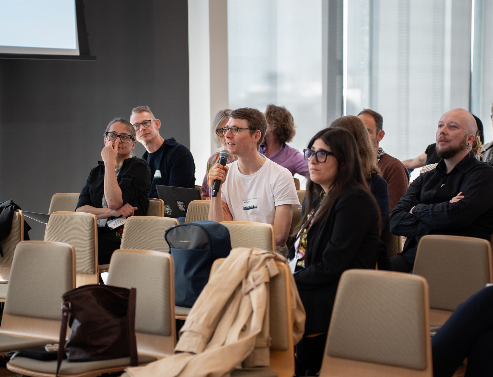 An audience with one member holding a microphone and speaking into it, while the rest of the audience looks forward.