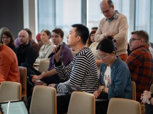 An audience looking attentively at one member holding a microphone and speaking into it.