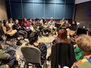 A group of scholars seated in a circle listening to one speak.