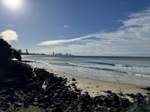 A beach with some rocks by the shore with a city in the distance.