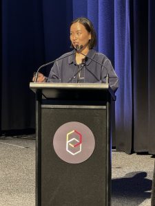 A woman standing behind a podium, speaking into a microphone on a stage.