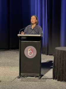 A woman standing behind a podium, speaking into a microphone on a stage.