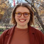 Corban Davis looks at the camera with fall trees behind her